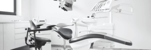 Modern dental office with a reclining dental chair, overhead light, equipment, and a stool on a clean, light-colored floor.