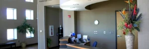Reception area of a medical office with a curved desk, computer, wall clock, and a large vase of flowers on the counter.