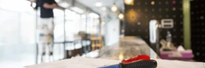 A screwdriver and building plans rest on a countertop with a worker on a ladder in the background.