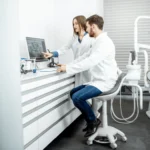 Two dentists in lab coats review a dental X-ray on a computer in a modern dental clinic.